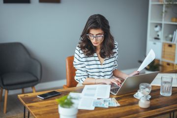 Woman at desk in front of laptop reading papers