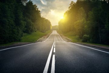 Roadmap; empty highway through forest at sunrise with sunlight shining through trees.