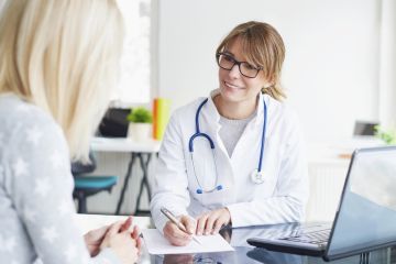 Smiling doctor talking with a patient in an office with a laptop and stethoscope on the desk.